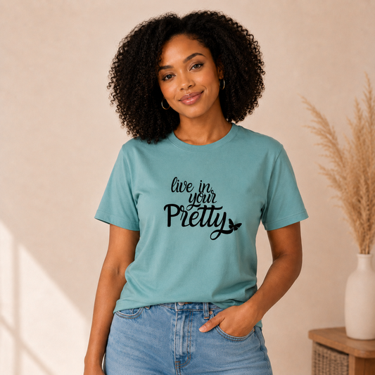 Black woman wearing a soft teal Live in Your Pretty graphic tee with black script lettering.
