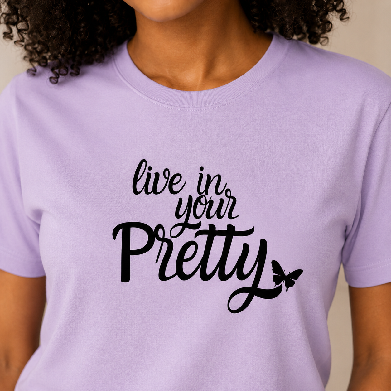 Close-up of the Live in Your Pretty black script design with butterfly detail on a soft lilac tee.